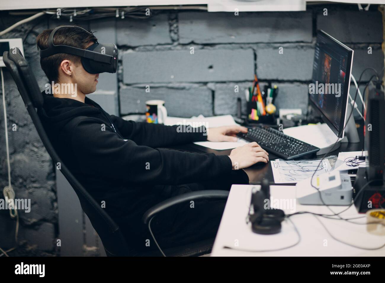 Jeune homme programmeur assis sur une chaise avec ordinateur de bureau près de lunettes de réalité virtuelle, casque vr lunettes. Banque D'Images