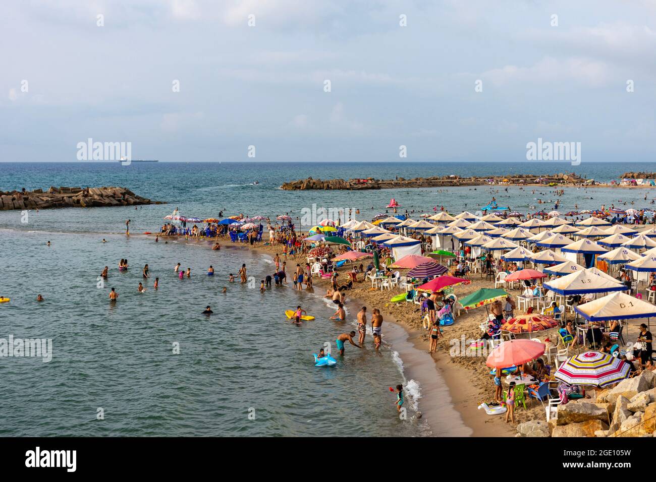 Vue en grand angle d'une foule de gens s'amuser sur la plage, enfants jouant dans l'eau, Skikda, Algérie. Banque D'Images Vue en grand angle d'une foule de gens s'amuser sur la plage, enfants jouant dans l'eau, Skikda, Algérie. Banque D'Images