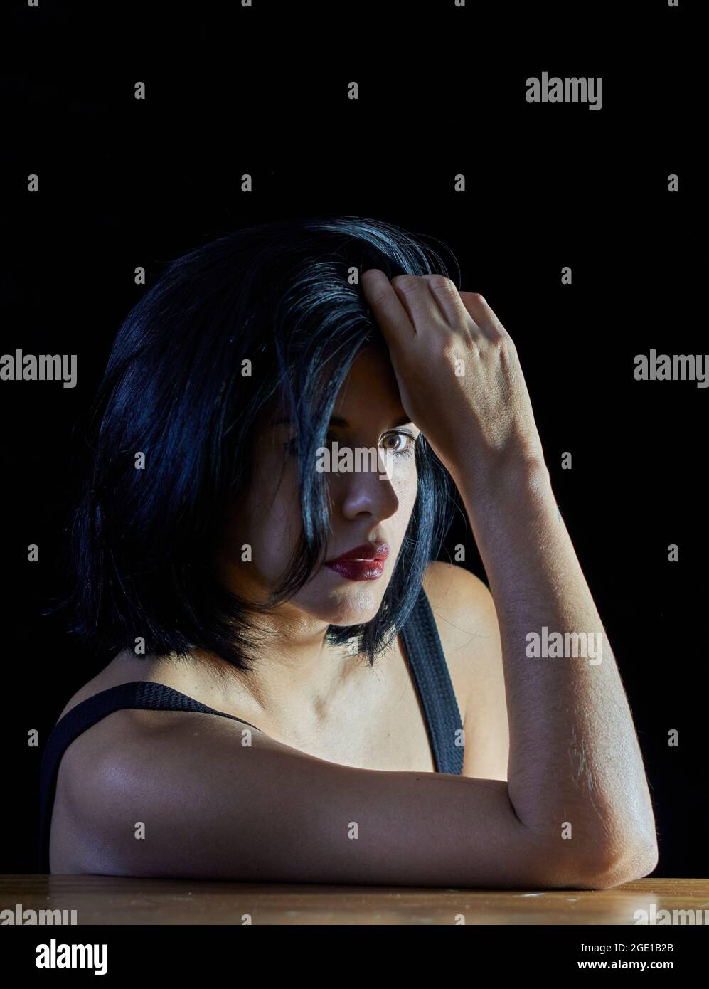 portrait d'une femme brune sérieuse regardant l'appareil photo avec une main touchant ses cheveux noirs. vertical Banque D'Images