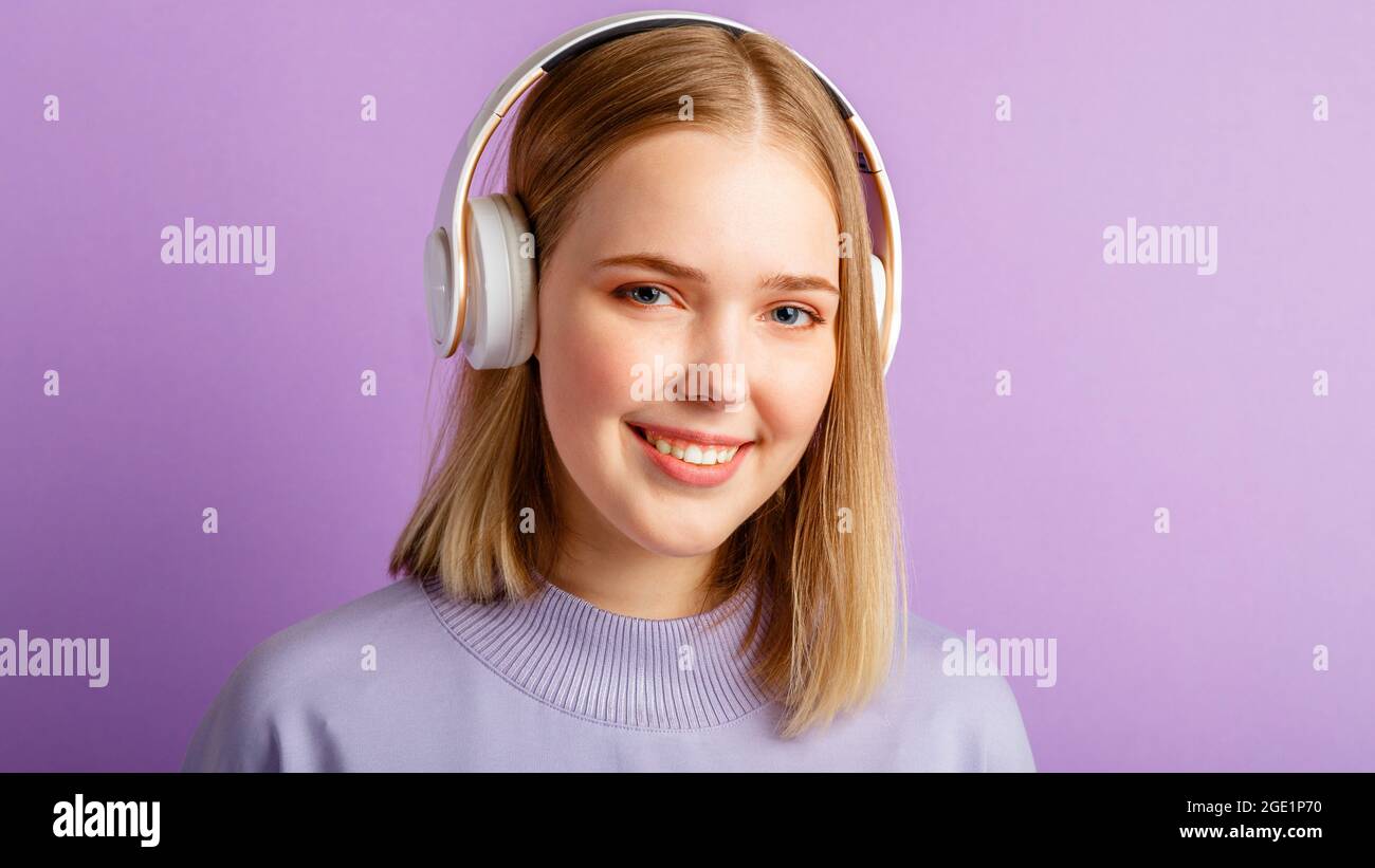 Bonne jeune femme dans le portrait de casque. Belle femme souriante avec une coiffure blonde Profitez de la musique de chanson dans un casque isolé au-dessus de violet Banque D'Images