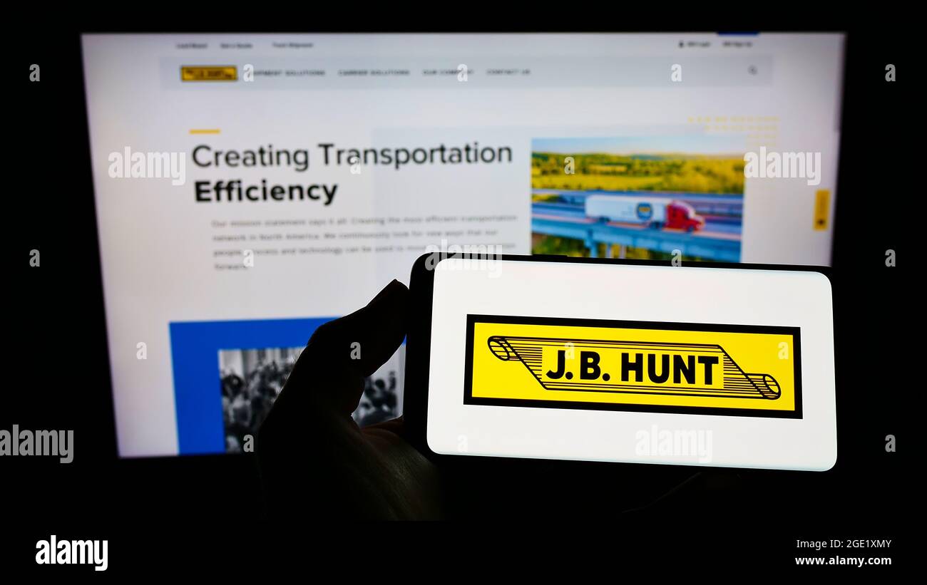 Personne portant un smartphone portant le logo de la société logistique J.B. Hunt transport Services Inc. À l'écran devant le site Web. Mise au point sur l'affichage du téléphone. Banque D'Images