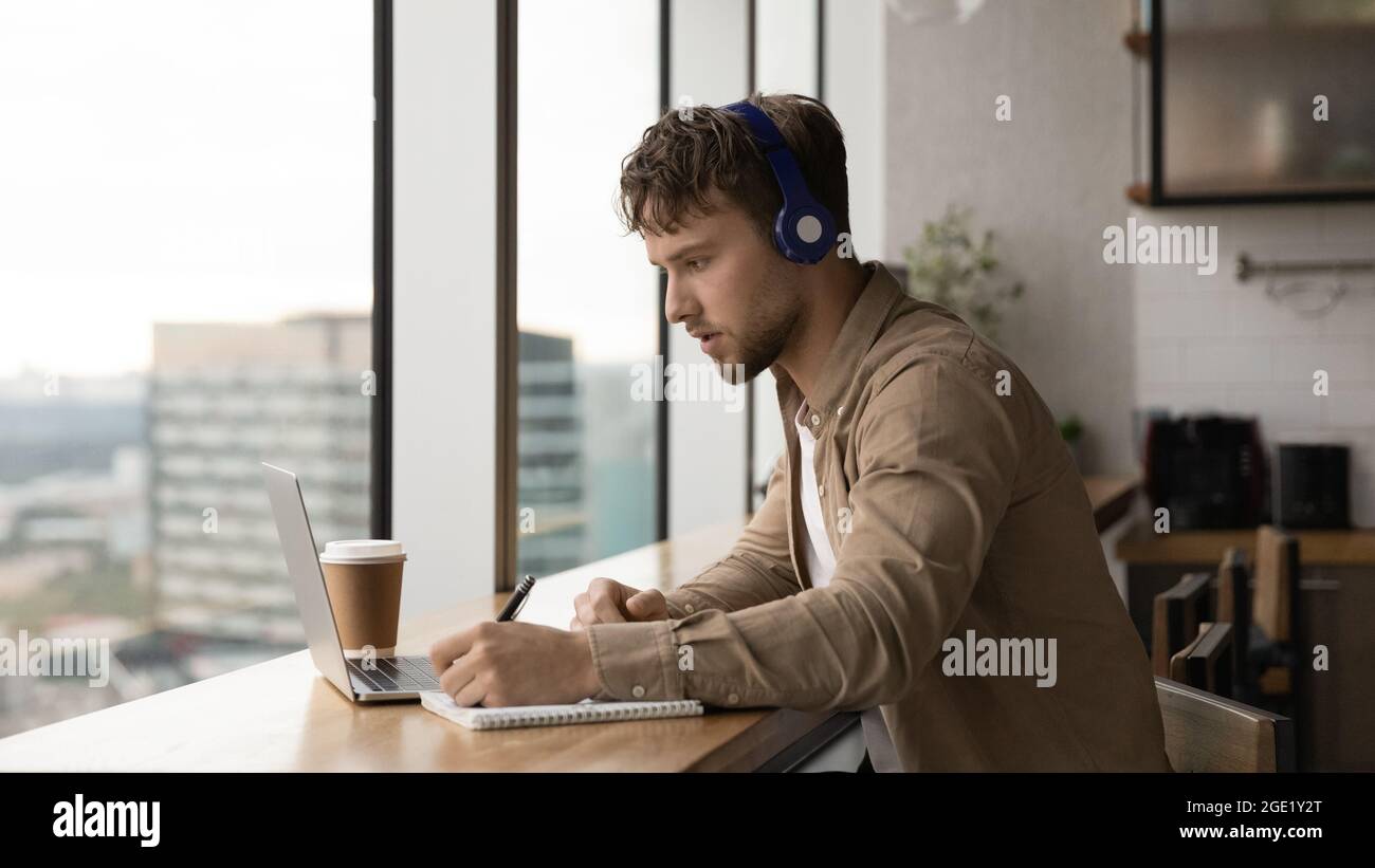 L'homme écoute l'audio prend des notes pour effectuer une tâche à l'aide d'un ordinateur portable Banque D'Images