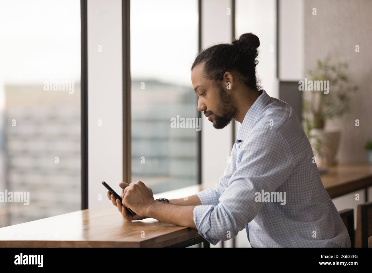 Un homme d'affaires africain sérieux assis sur le lieu de travail tient le smartphone vérifier l'e-mail Banque D'Images