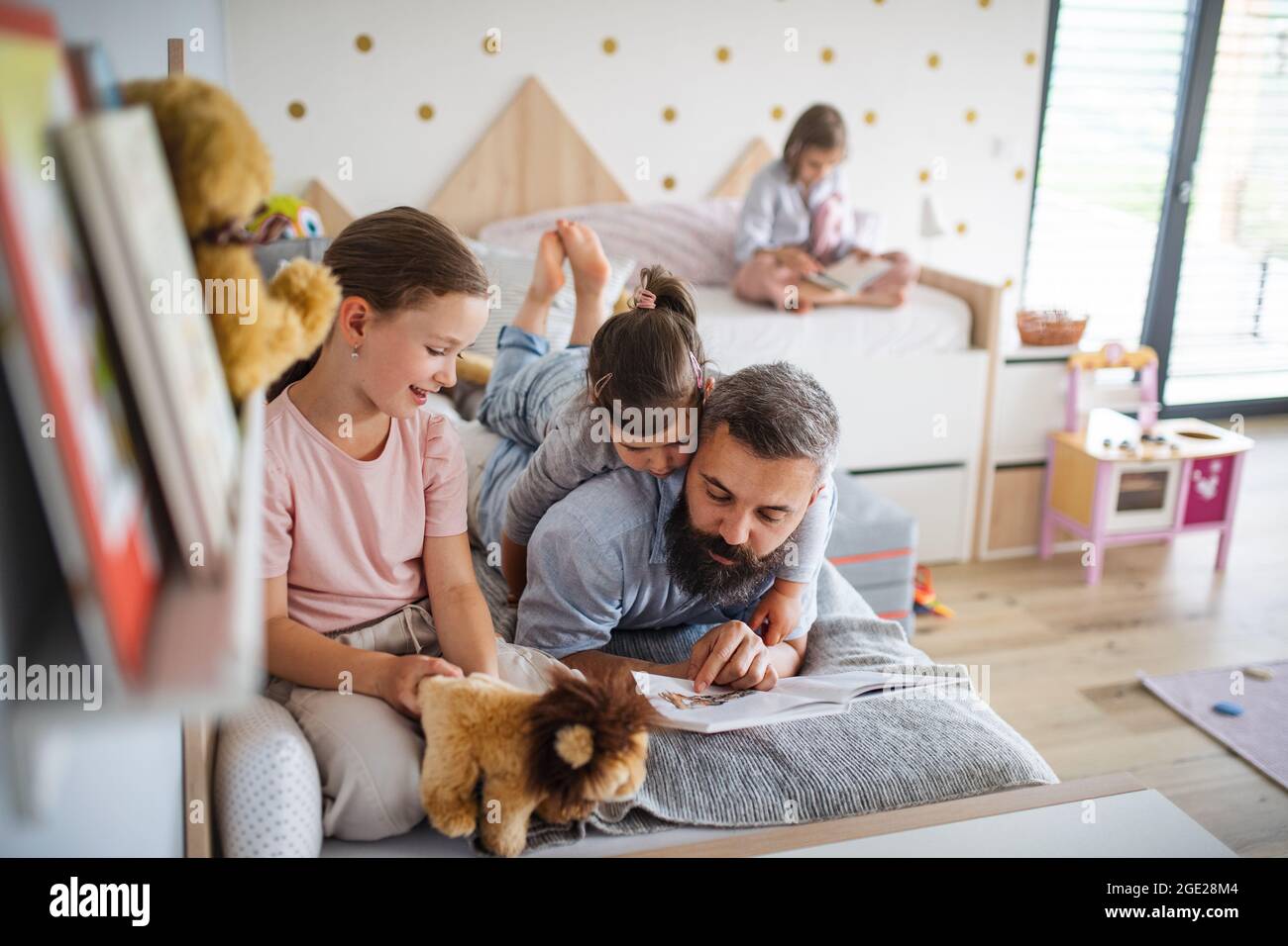 Père avec trois filles à l'intérieur à la maison, lisant un livre. Banque D'Images