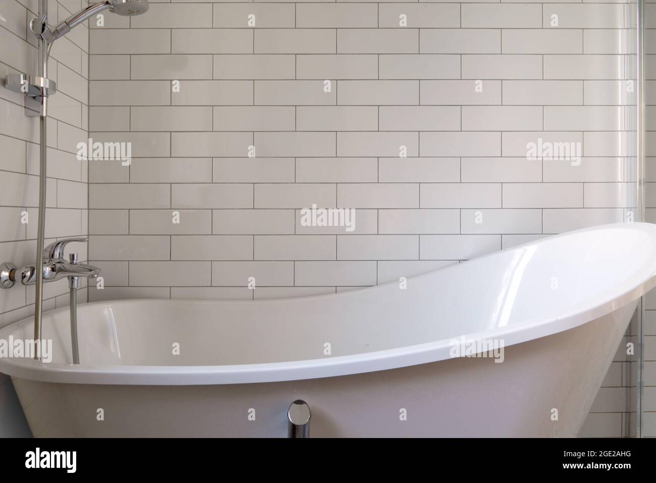 Baignoire vide avec un robinet à pomme de douche et un drain dans la salle de bains blanche sur un fond de carreaux de briques Banque D'Images