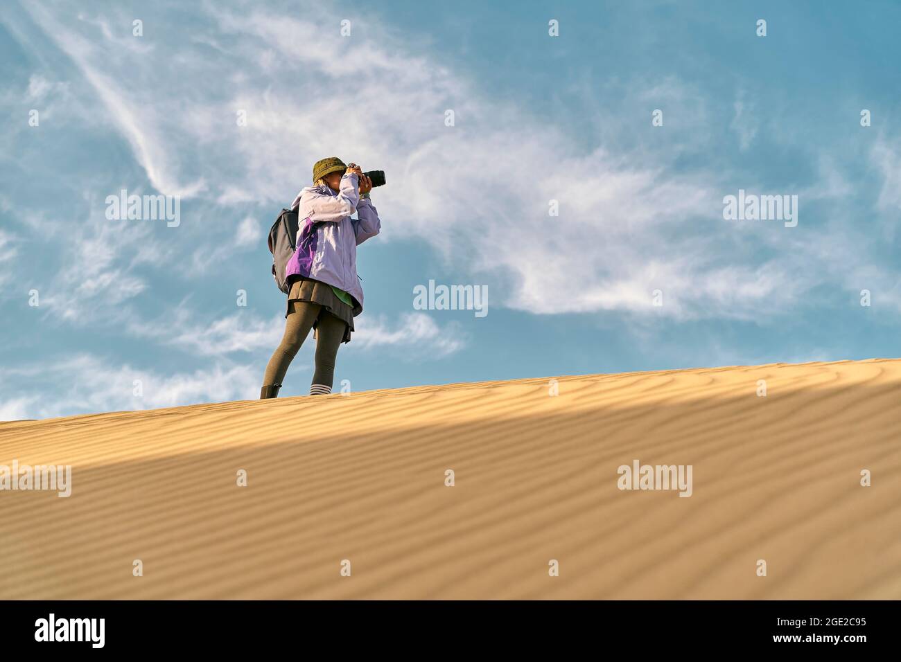 photographe asiatique debout au-dessus d'une dune de sable prenant une photo Banque D'Images