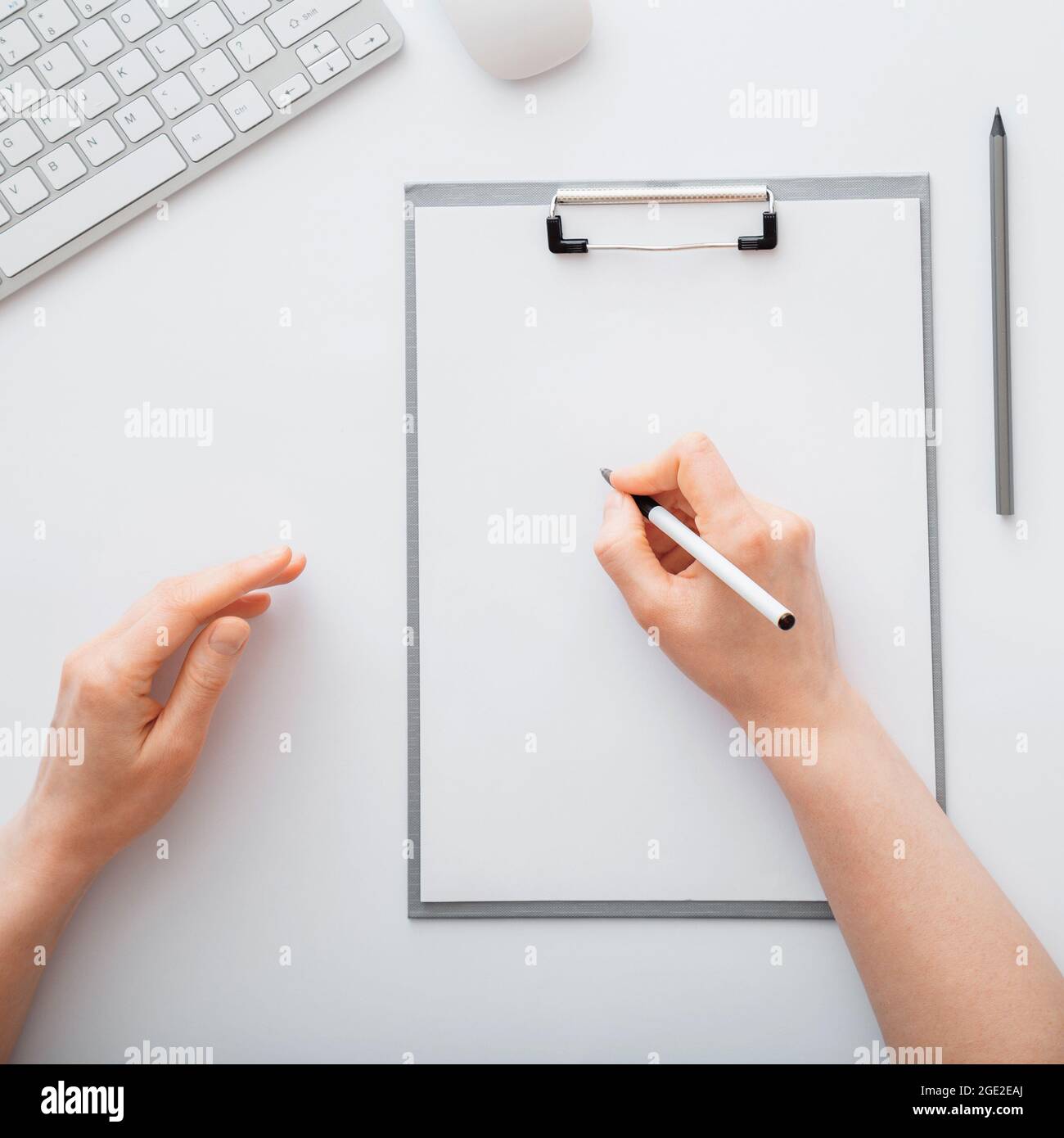 Main féminine prenant des notes sur le papier sur la table de travail blanche dans l'espace de travail. Vue de dessus Banque D'Images