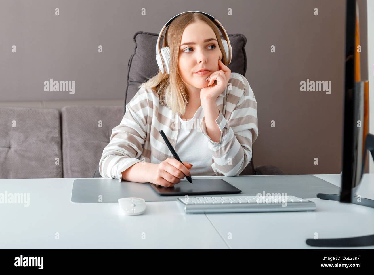 Pensive jeune femme freelance réfléchit sur la résolution de problème. Le concepteur utilise une tablette graphique lorsqu'il travaille. Artiste numérique femme dans le casque fonctionne avec Banque D'Images