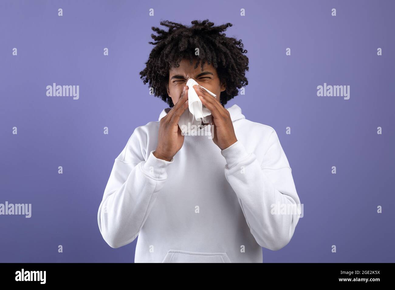 Rhume et grippe. Adolescent noir malade éternuant dans des tissus en papier, souffrant de rhinite ou de sinusite sur fond violet Banque D'Images