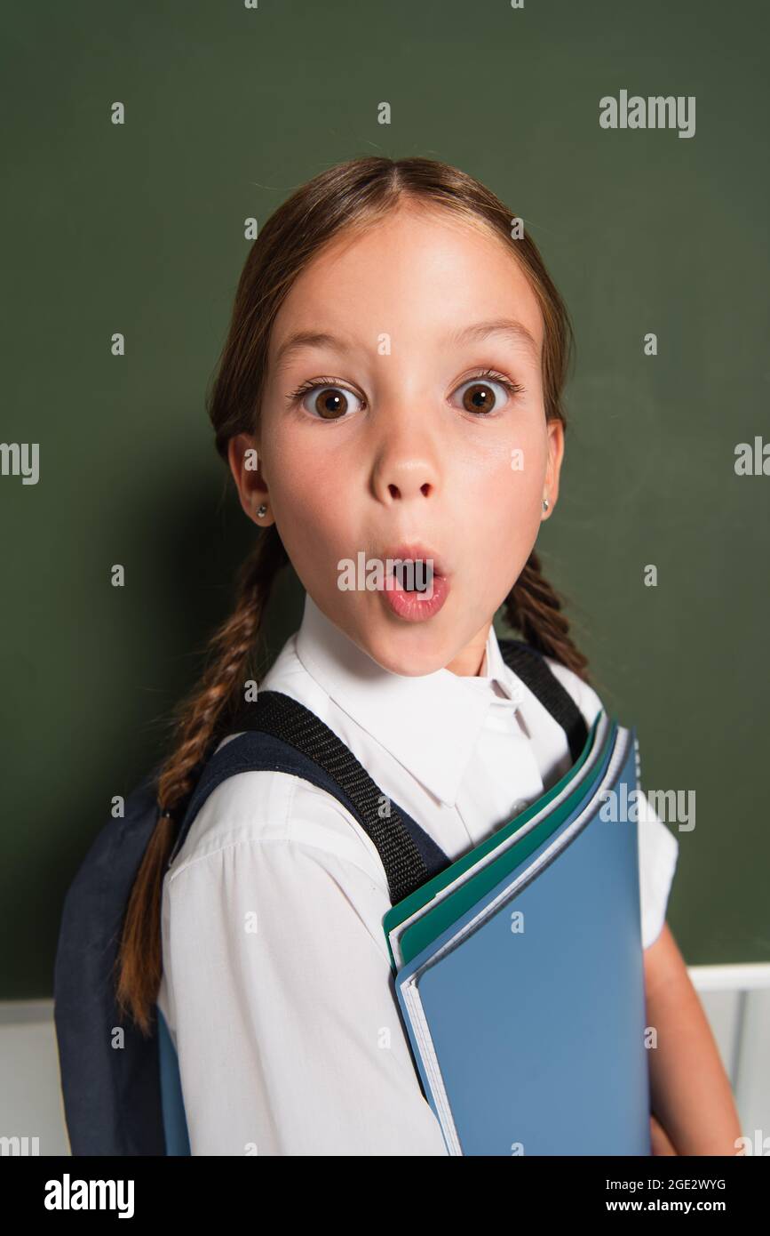 un enfant écolier ravie avec des photobooks qui regardent l'appareil photo près du tableau noir sur fond gris Banque D'Images