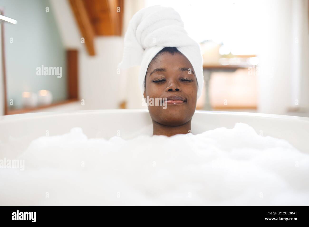Femme afro-américaine souriante dans la salle de bains se détendant dans la salle de bains avec les yeux fermés Banque D'Images