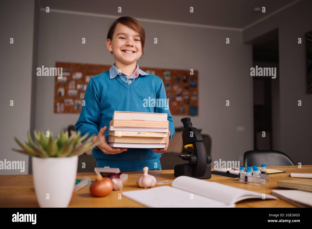 Formation en ligne à distance, apprentissage sur Internet. Garçon de première classe étudiant à la maison, tenant un tas de livres, se préparer pour la leçon en ligne Banque D'Images