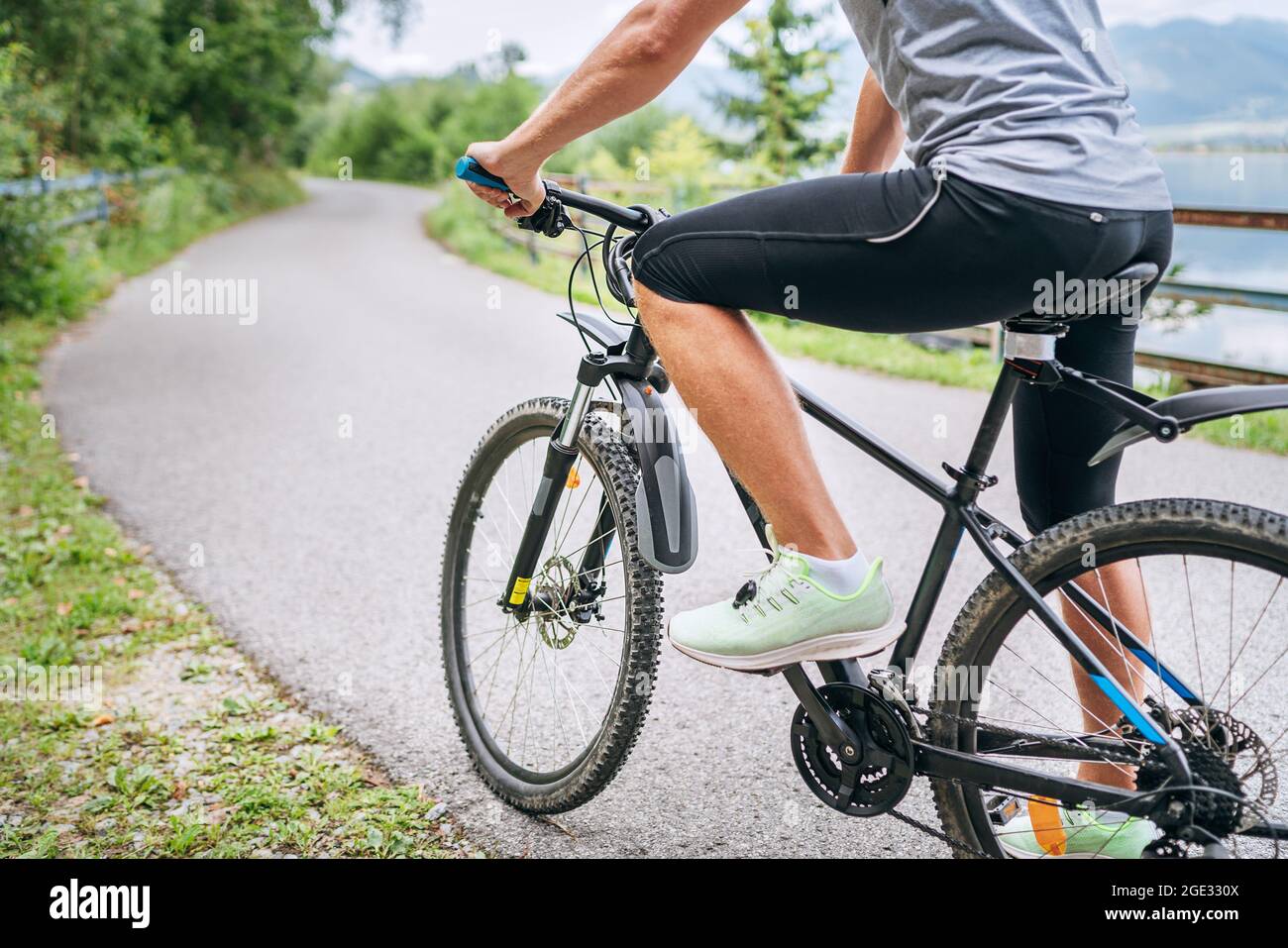 Photo en gros plan d'un homme vêtu de vêtements de cyclisme qui commence à  monter sur un vélo moderne sur la piste cyclable en asphalte de l'extérieur  de la ville. Les sportifs