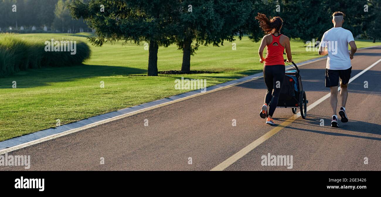 Couple de course avec enfant dans une poussette de jogging dans le parc public au lever du soleil. Course matinale pour toute la famille Banque D'Images