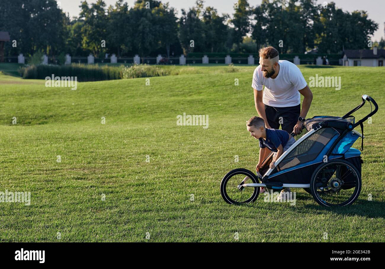 Père jouant et communiquant avec son enfant dans la poussette de bébé tout en se tenant sur une pelouse verte par un jour ensoleillé. Le père et le fils de la famille, la da du père Banque D'Images