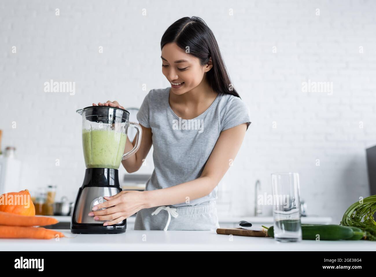 joyeuse femme asiatique préparant un smoothie de légumes dans un shaker électrique Banque D'Images