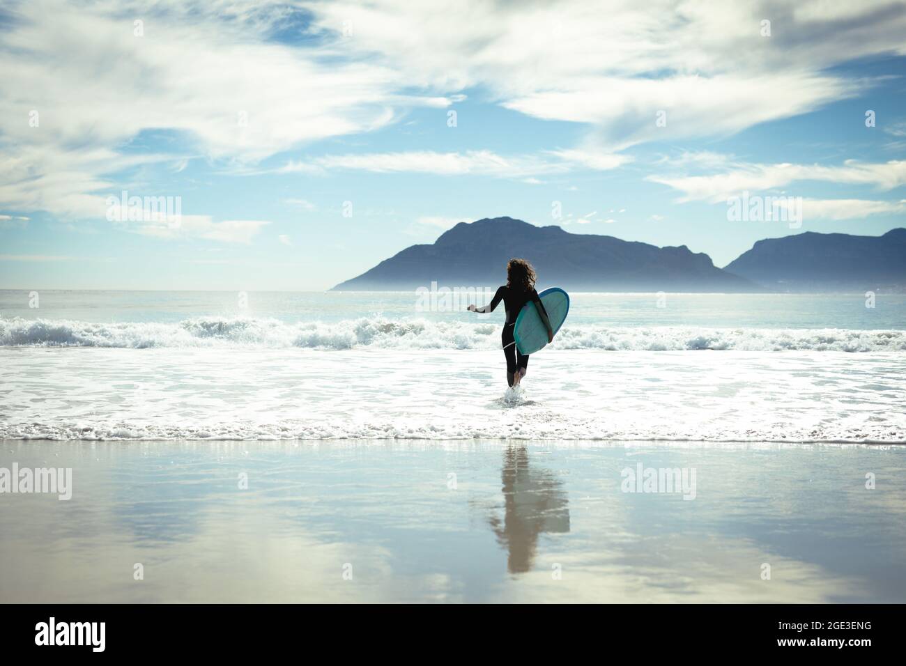 Femme de race mixte tenant une planche de surf en mer le jour ensoleillé Banque D'Images