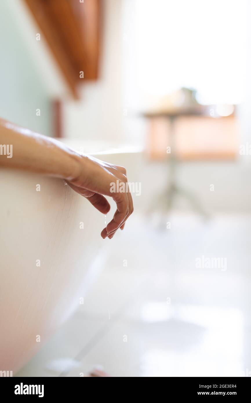 Main de la femme de race mixte dans la salle de bains se relaxant dans le bain Banque D'Images