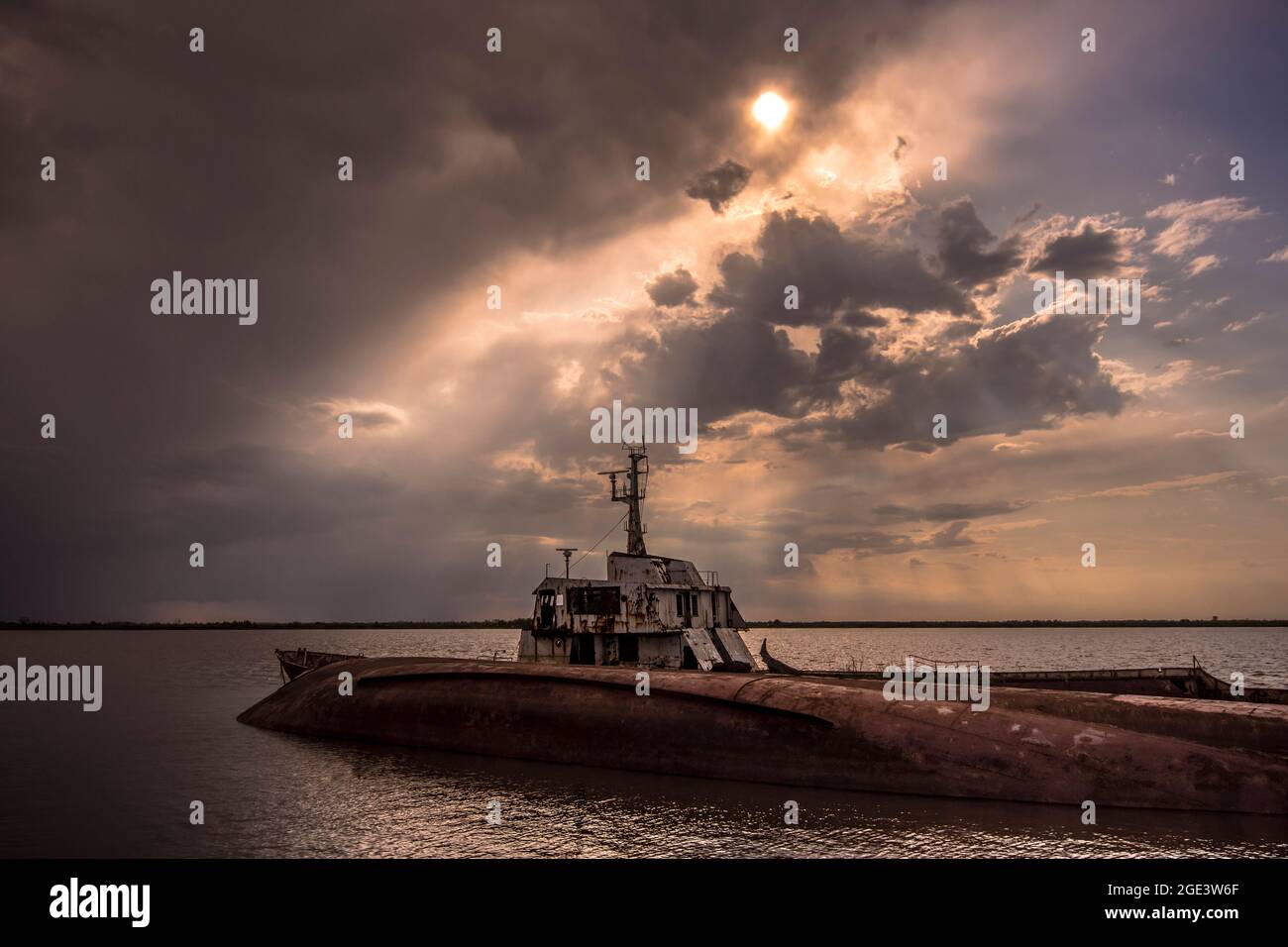 bateau abandonné dans l'eau avec un ciel spectaculaire avec le soleil derrière les nuages Banque D'Images