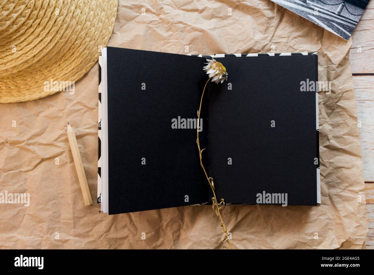 Composition de pose à plat avec carnet noir vierge ouvert, crayon, carte postale noir-blanc, lavande séchée et chapeau de paille sur fond de papier artisanal. Vue de dessus. Banque D'Images