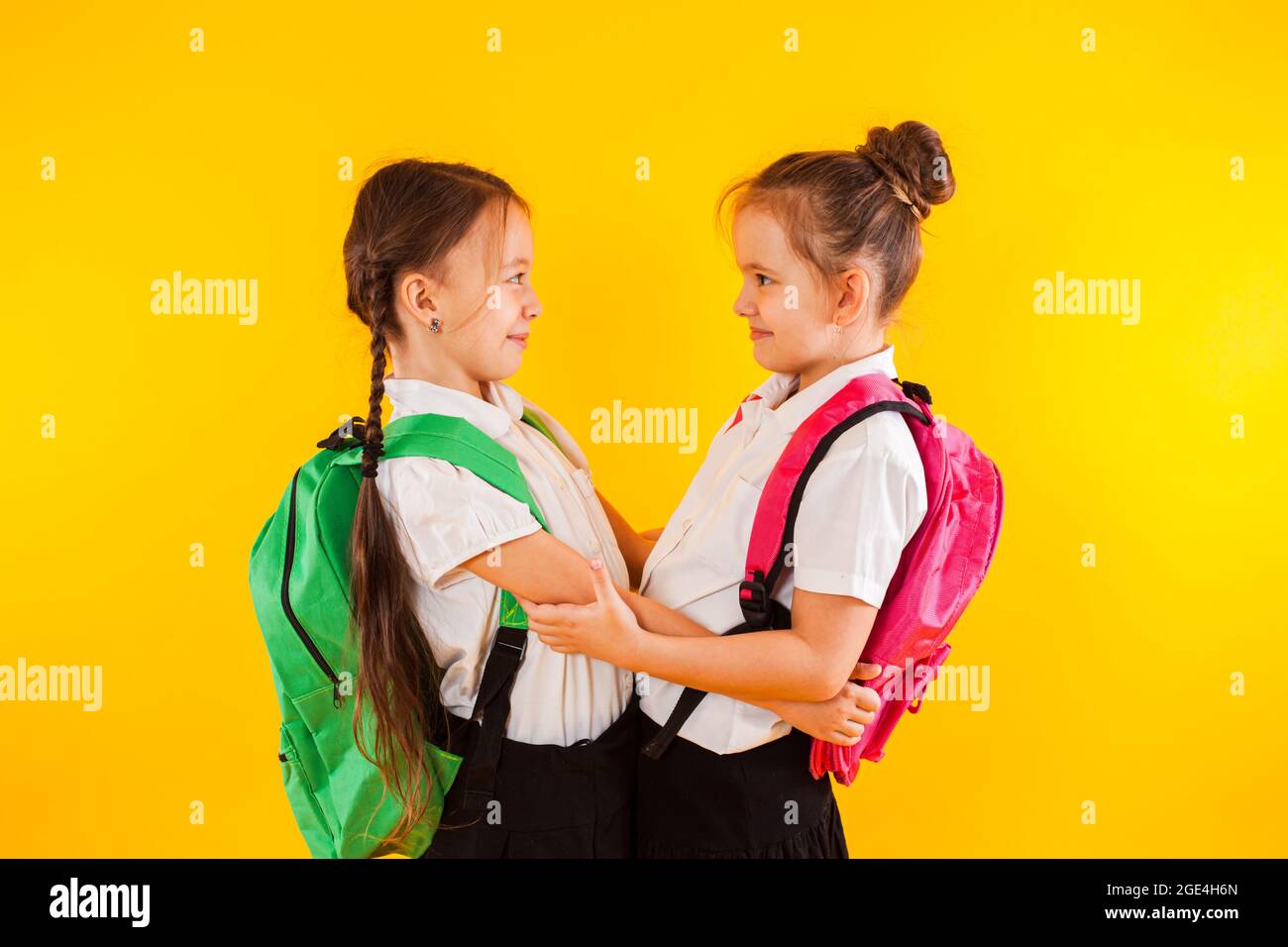 Deux filles d'école souriantes en uniforme s'embrasent au jaune Banque D'Images