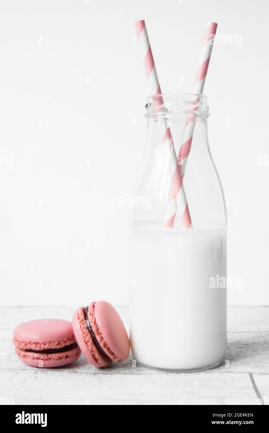 Petite bouteille de lait en verre avec pailles en papier rose à rayures et macarons roses Banque D'Images