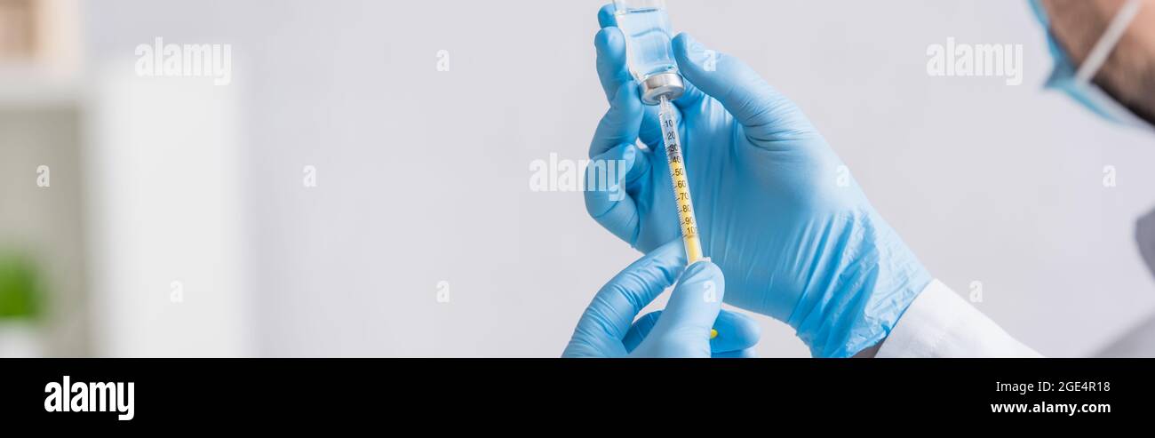 vue partielle du médecin dans des gants en latex bleu remplissant la seringue avec le vaccin coronavirus, bannière Banque D'Images