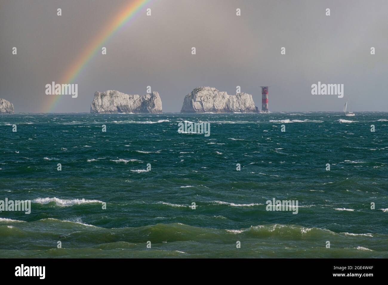 Voile dans le Solent juste au large des aiguilles des manteaux de l'île de Wight avec un arc-en-ciel dans le ciel orageux Banque D'Images