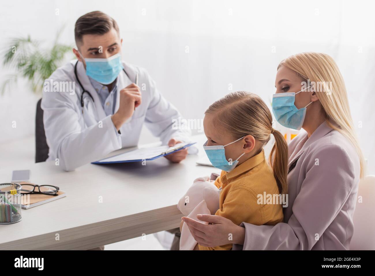 Mère dans le masque médical regardant la fille avec le jouet doux près de pédiatre Banque D'Images