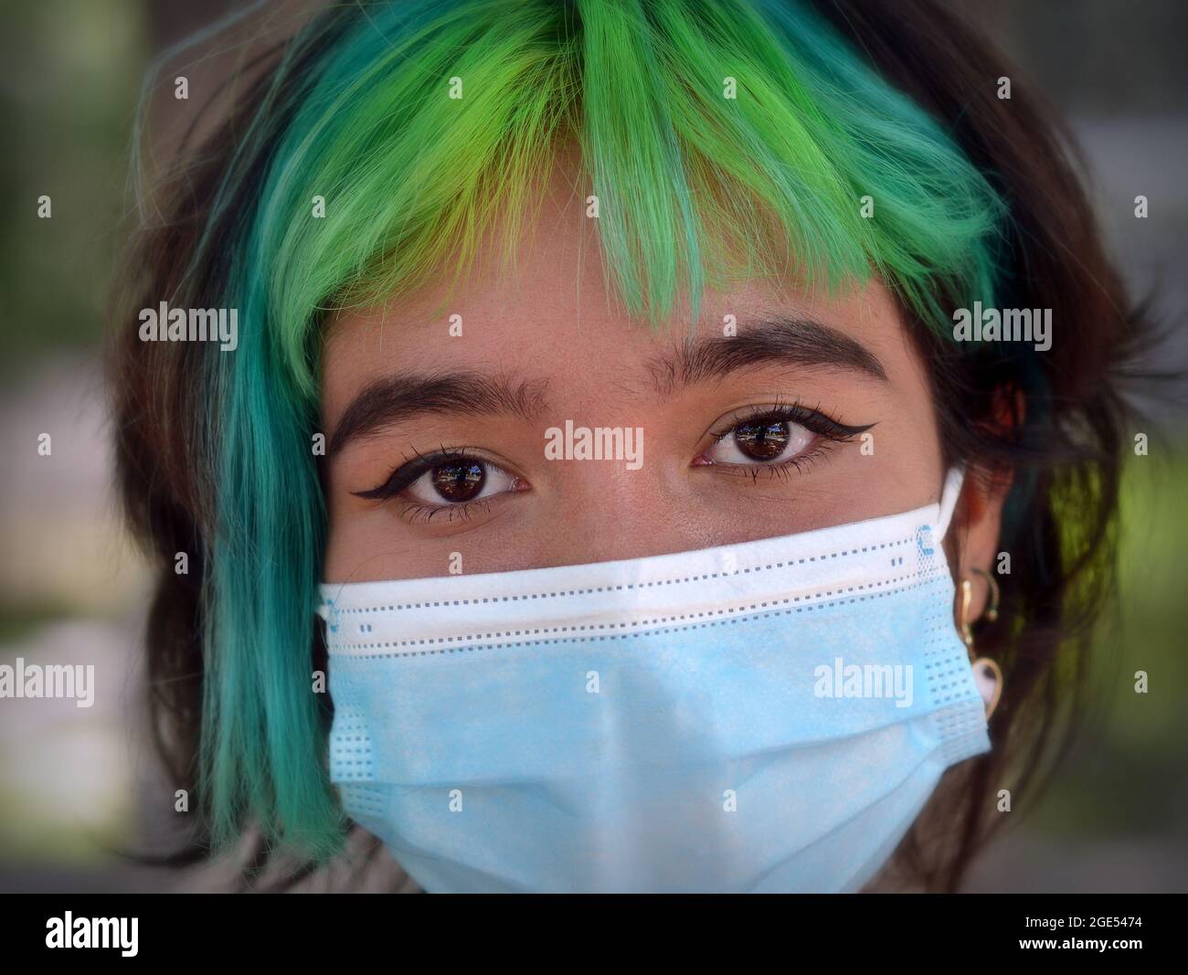 Une jeune fille caucasienne aux yeux bruns et aux cheveux teints en vert et en bleu porte un masque chirurgical bleu clair pendant la pandémie mondiale du coronavirus. Banque D'Images
