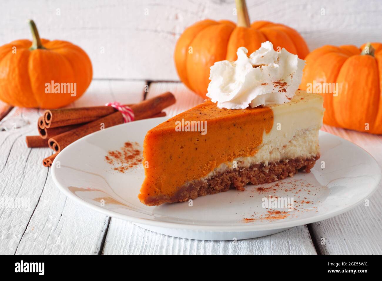 Tranche de gâteau au fromage à la citrouille avec crème fouettée, vue latérale sur une scène de table sur fond de bois blanc. Banque D'Images