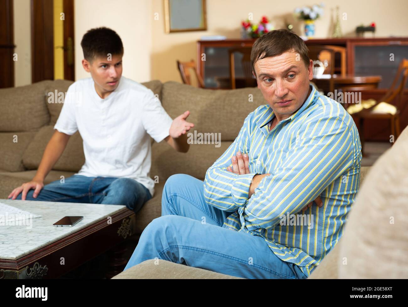 Un père contrarié assis tout en se querellant avec son fils adolescent Banque D'Images