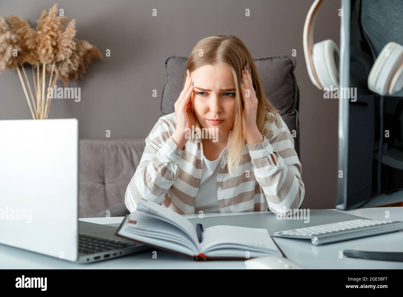 Une jeune femme en situation de stress travaille au bureau via un ordinateur portable. Jeune femme fatiguée avec mal de tête en raison de la date limite d'heures supplémentaires problème. L'étudiant souffre de l'e-apprentissage Banque D'Images