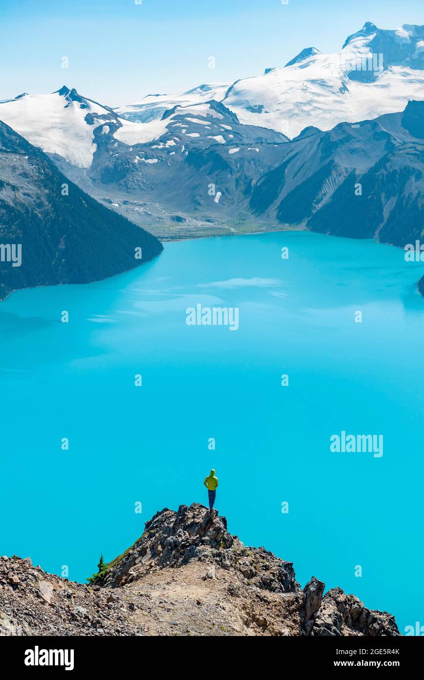 Jeune homme debout sur un rocher, regardant au loin, vue sur les montagnes et le glacier avec le lac bleu turquoise Garibaldi Lake, Peaks Panorama Ridge Banque D'Images