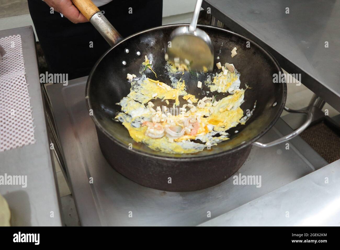 Vue en grand angle des aliments sautés. Œufs, crevettes et morceaux de tofu en cours de cuisson dans un wok en fer noir. Banque D'Images