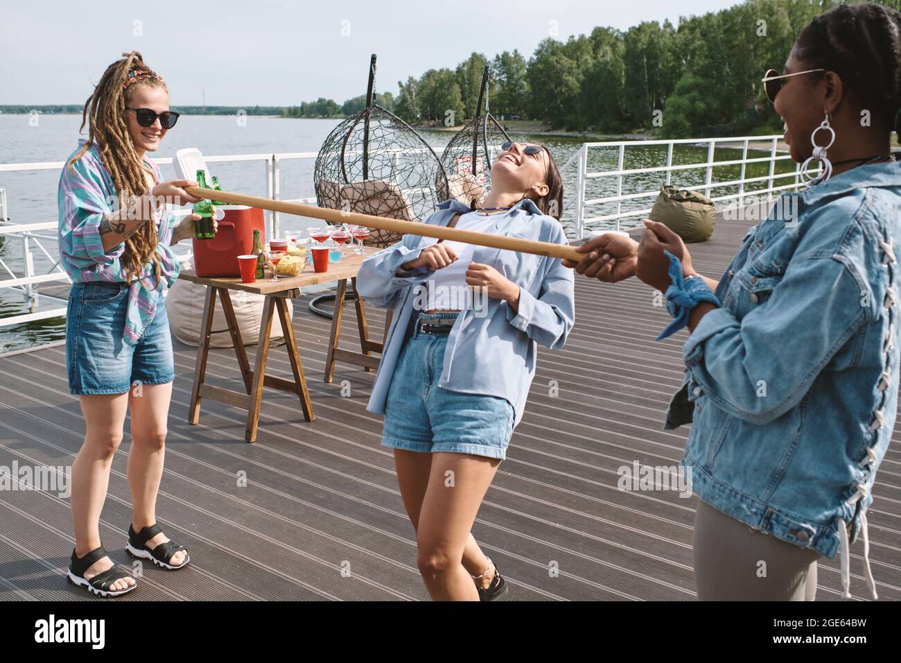 Joyeuse jolie jeune femme en lunettes de soleil en appréciant jouer au jeu de limbo avec ses amis à la fête d'anniversaire Banque D'Images