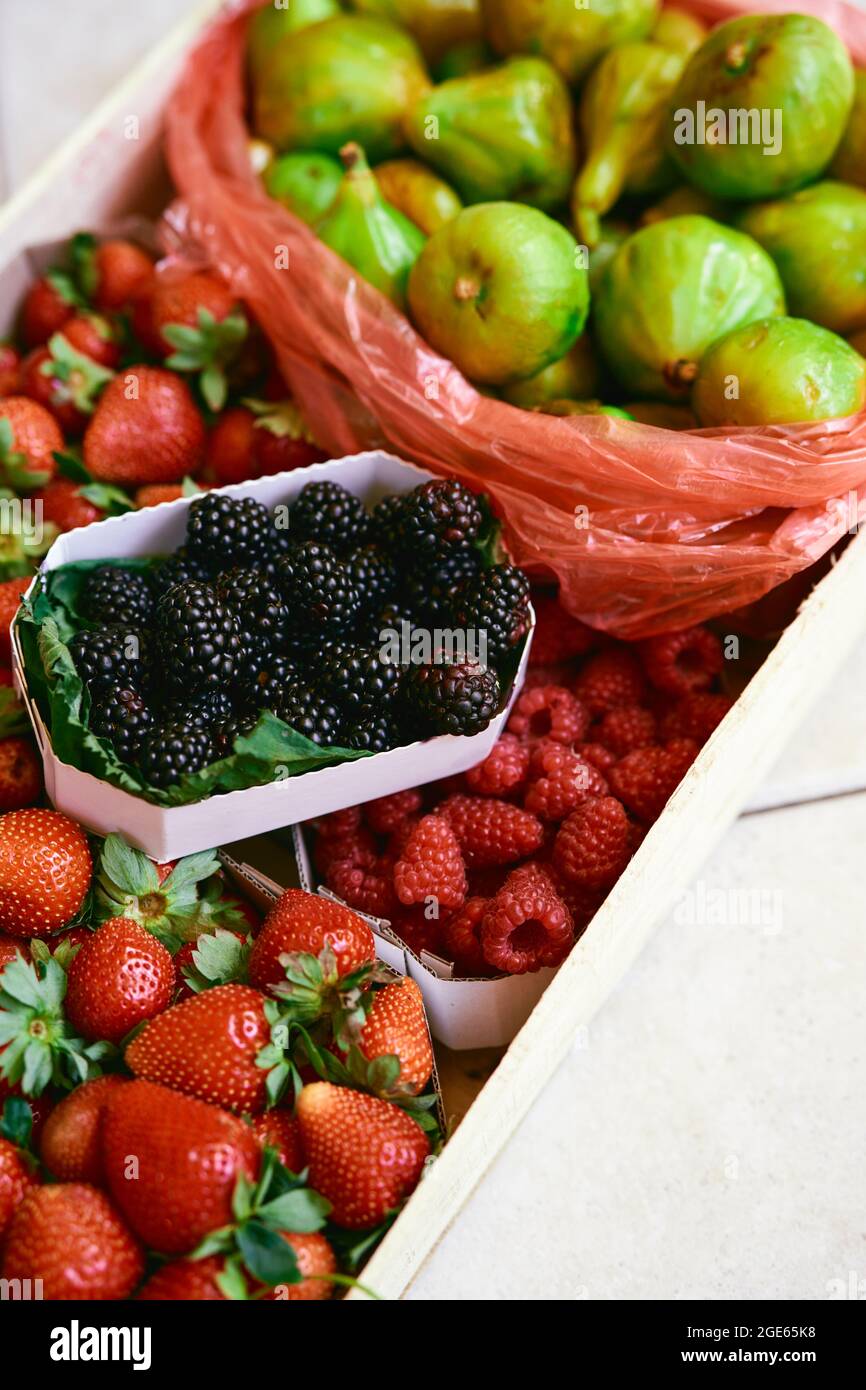 Un coffret en bois avec des boîtes de fraises, framboises, figues et mûres se trouve sur une tuile Banque D'Images