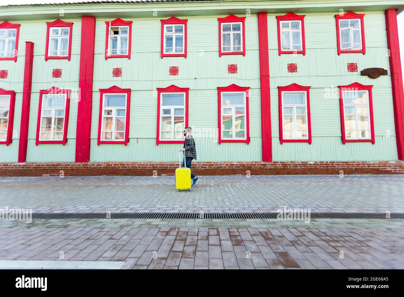 Portrait du côté du corps complet d'un homme de voyage heureux avec une valise marchant le long du bâtiment en ville. Banque D'Images