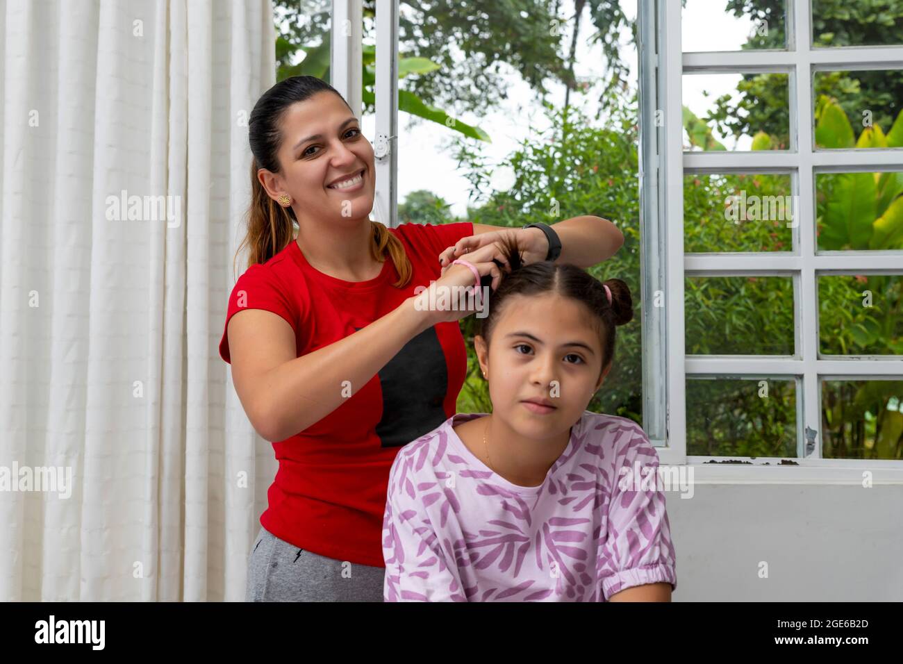 Latino mère coiffant les cheveux de la fille et regardant l'appareil photo Banque D'Images