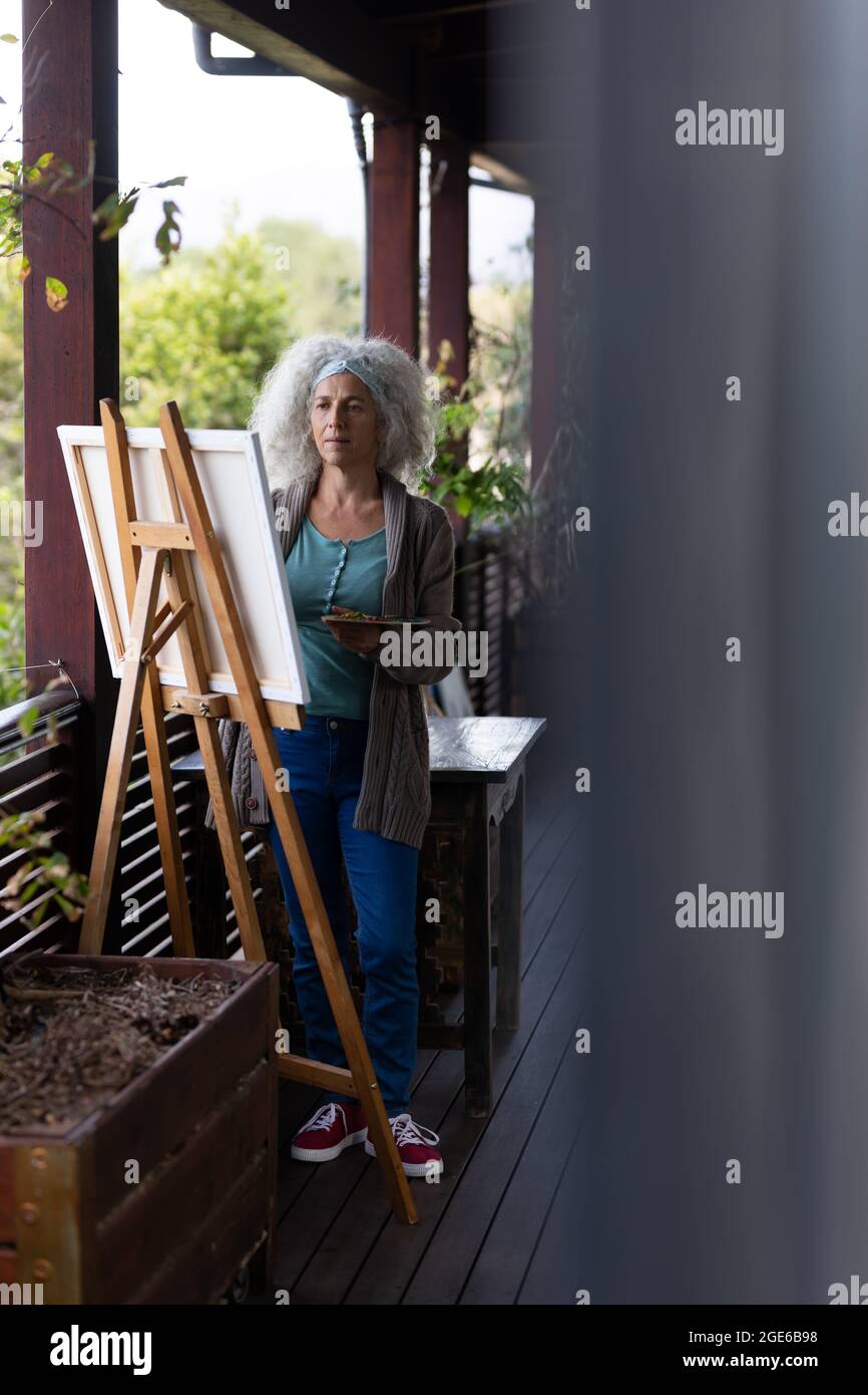 Femme caucasienne senior debout sur un balcon ensoleillé et peinture Banque D'Images