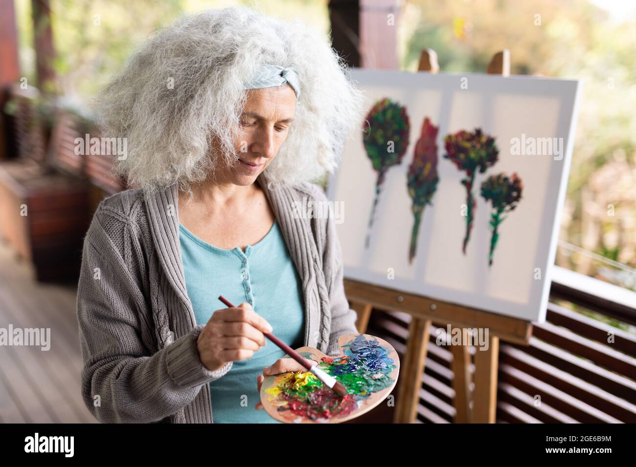 Femme caucasienne senior debout sur un balcon ensoleillé et peinture Banque D'Images