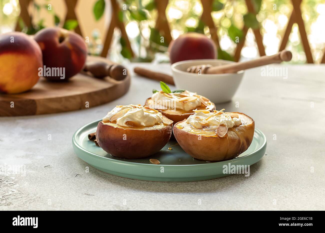 Pêches cuites à la cannelle, aux pétales d'amande, au fromage à la crème et au miel sur un fond de béton léger. Fruits dans une assiette à la menthe, vue de dessus, espace de copie. Banque D'Images