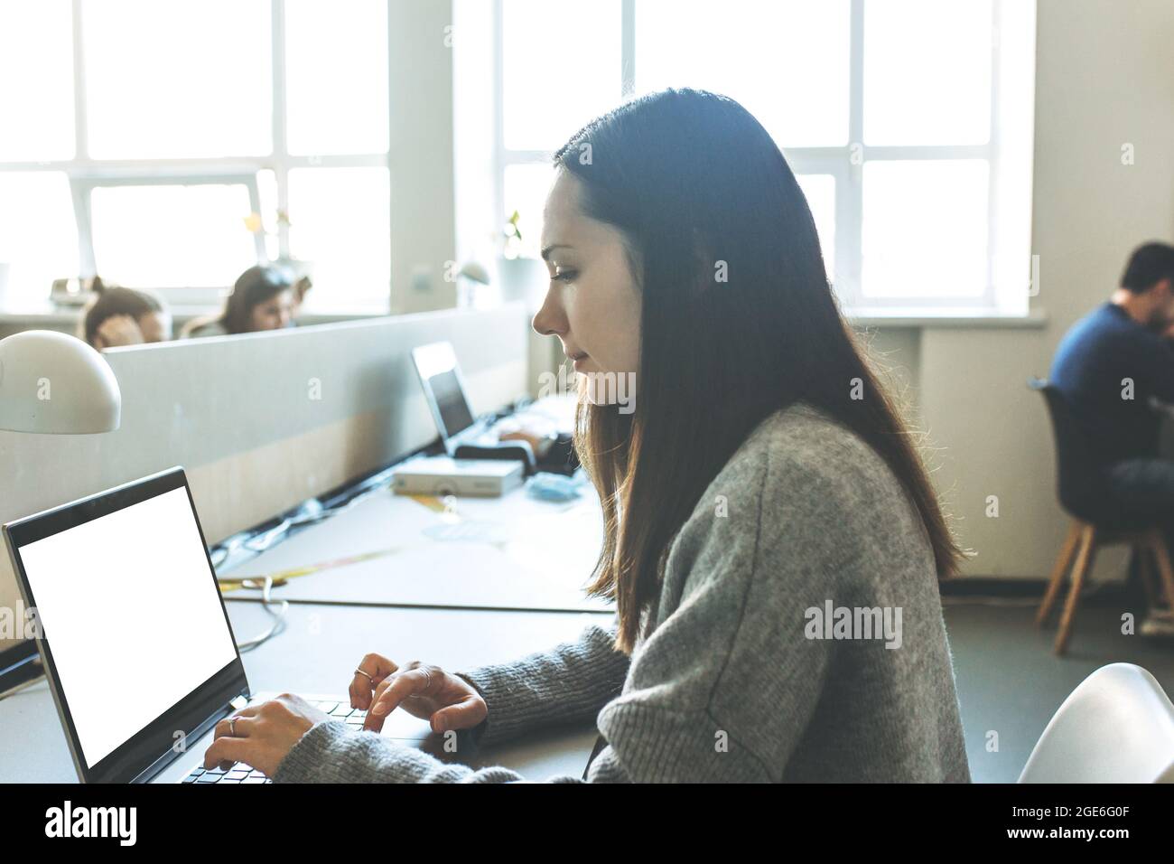 Une fille adulte utilise un ordinateur portable avec un écran blanc vierge pour la maquette Banque D'Images