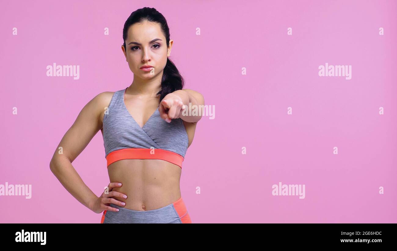 serious sportswoman debout avec la main sur la hanche et pointant avec le doigt isolé sur le rose Banque D'Images