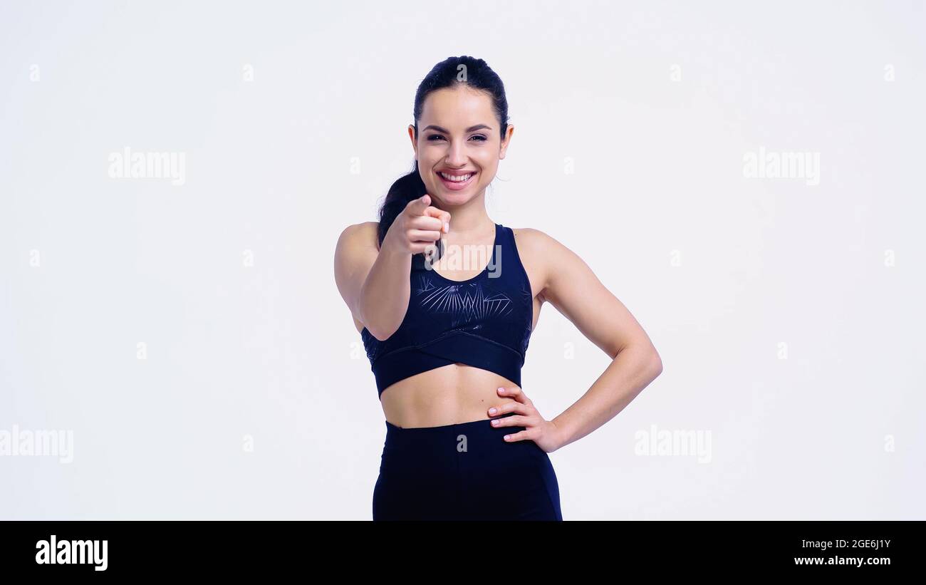 souriant sportswoman pointant avec le doigt tout en se tenant avec la main sur la hanche isolée sur blanc Banque D'Images
