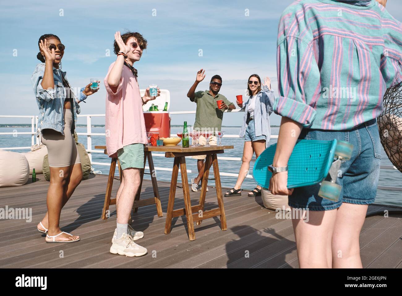 Groupe de jeunes heureux de voir leur ami avec le skateboard à la fête sur la jetée au bord du lac Banque D'Images