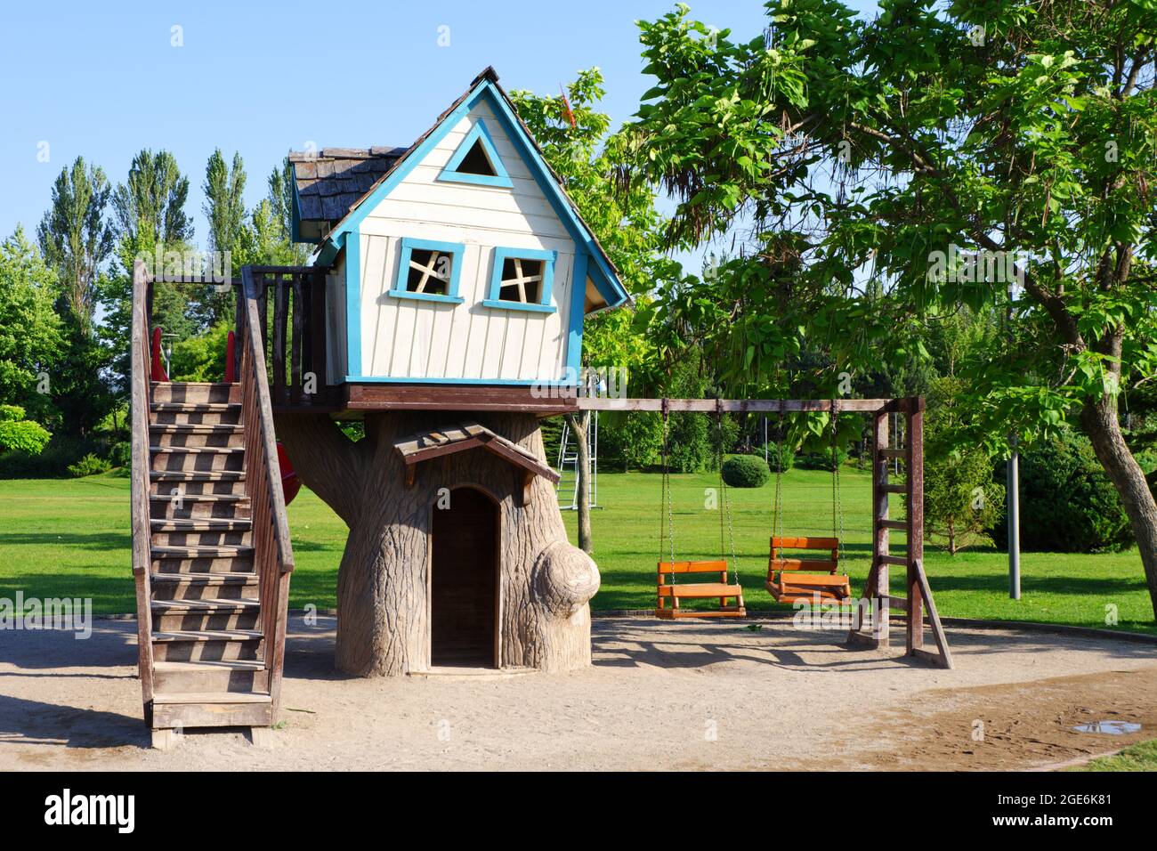 Petite maison en bois blanc avec fenêtres bleu clair et balançoires en bois avec arbres Banque D'Images