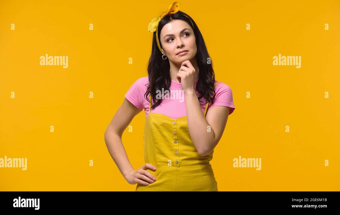 Femme pensive tenant la main sur la hanche isolée sur le jaune Banque D'Images