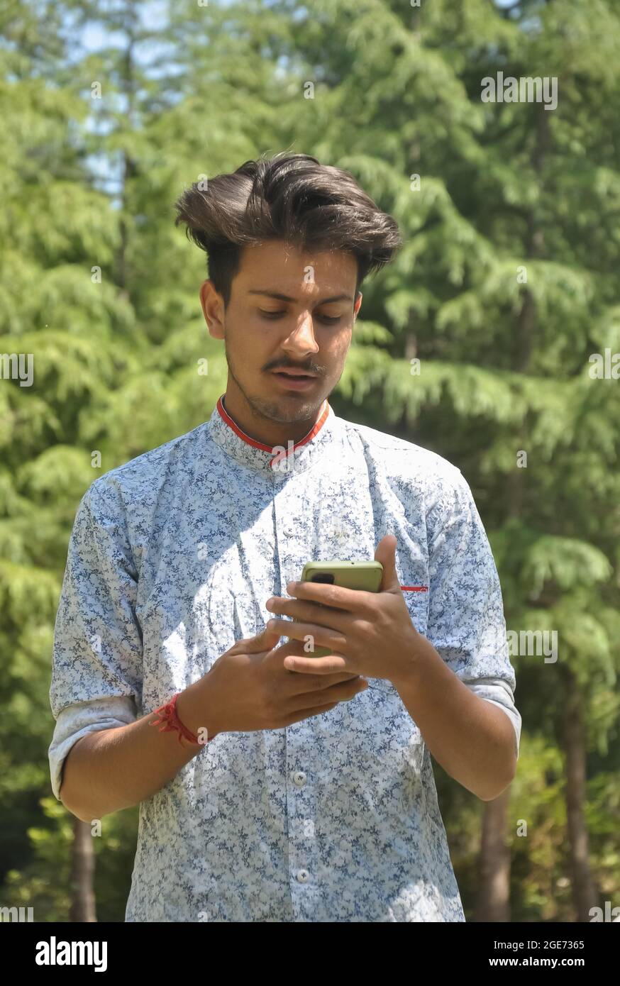 Portrait d'un jeune garçon indien beau debout à l'extérieur avec l'utilisation du téléphone mobile Banque D'Images