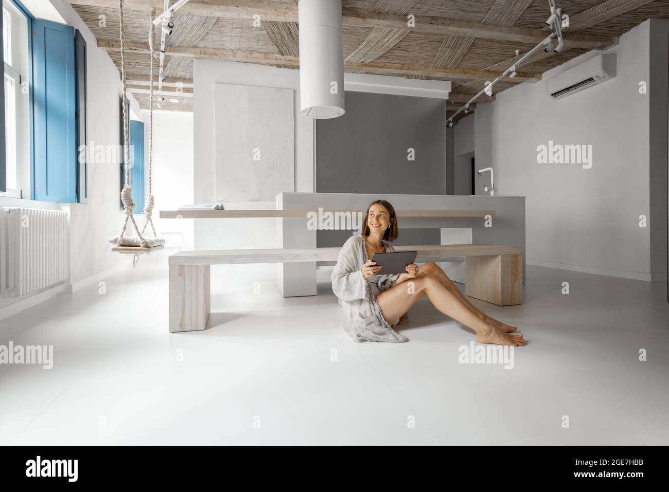 Une jeune femme travaille sur une tablette numérique tout en étant assise au sol dans un studio moderne. Travail à distance depuis le confort et la modernité de la maison Banque D'Images